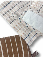 Close-up of a woven textile product, likely a pouch or sleeve, showing a cream and tan plaid pattern with thin dark blue lines, a white textured insert, and a brown section with white vertical stripes.